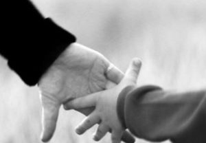 Black and white photo of child going to hold an adult's hand.